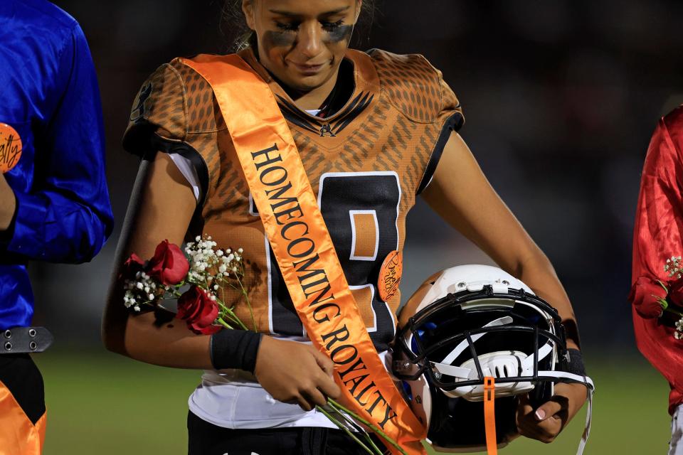 Atlantic Coast's Gaby Rourke (19) looks at her sash and roses, honored to be named Junior Homecoming Queen, while carrying her football helmet near midfield during halftime of Friday's game against Raines.