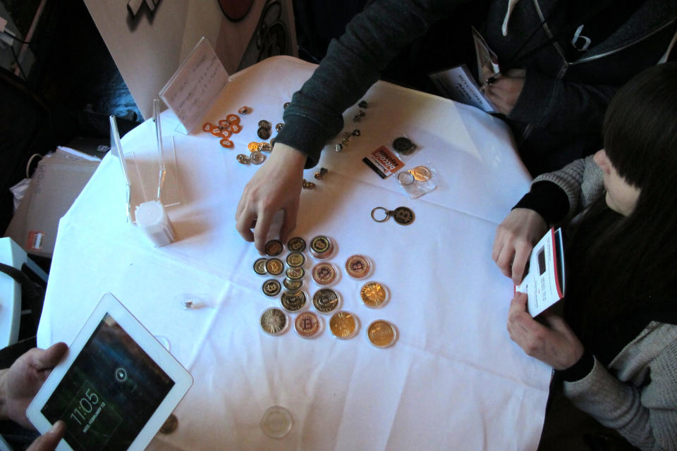 Attendees of the Inside Bitcoins conference in Berlin examine Bitcoin buttons on Wednesday, Feb. 12, 2014. The conference brought together entrepreneurs and enthusiasts of the virtual currency to discuss business opportunities and recent developments. (AP Photo/Frank Jordans)