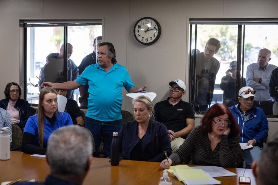 A man stands to speak at the golf meeting.