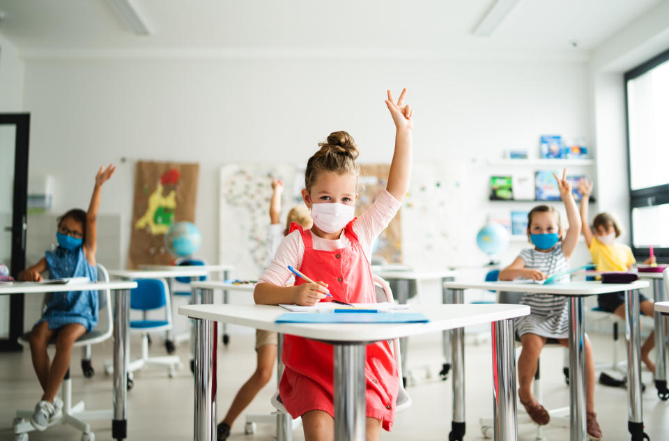 Boys and girls sitting at desks, raising hands.