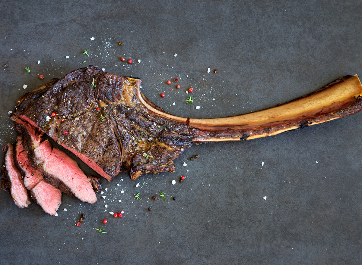 Sliced tomahawk steak with flecks of salt on a gray background