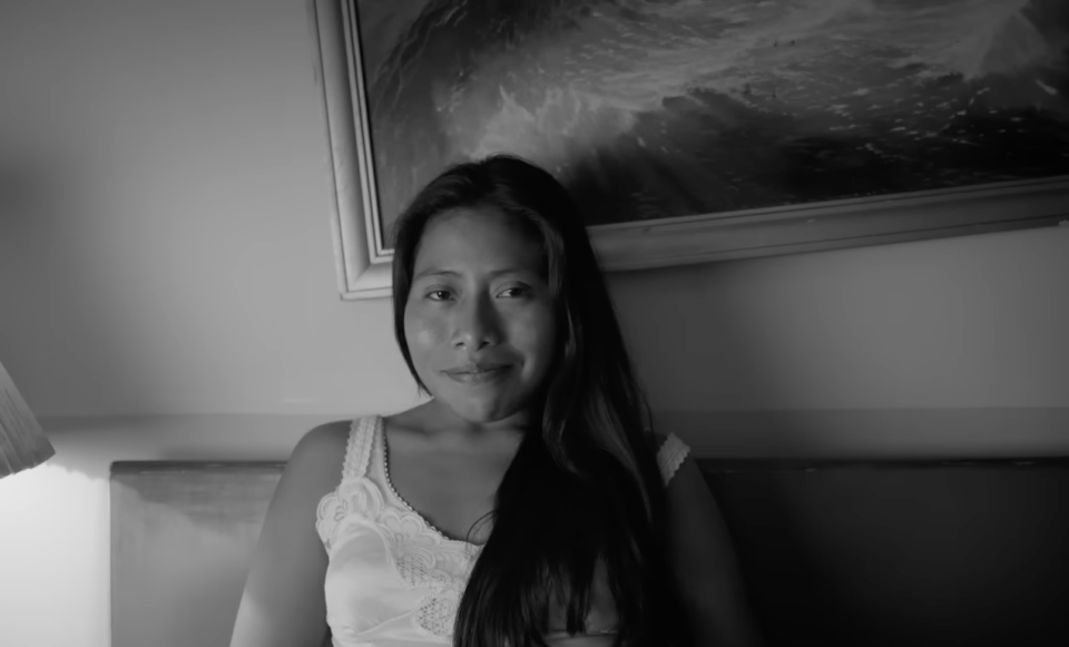 A black-and-white still of a woman sitting on a bed and smiling, from the movie ROMA