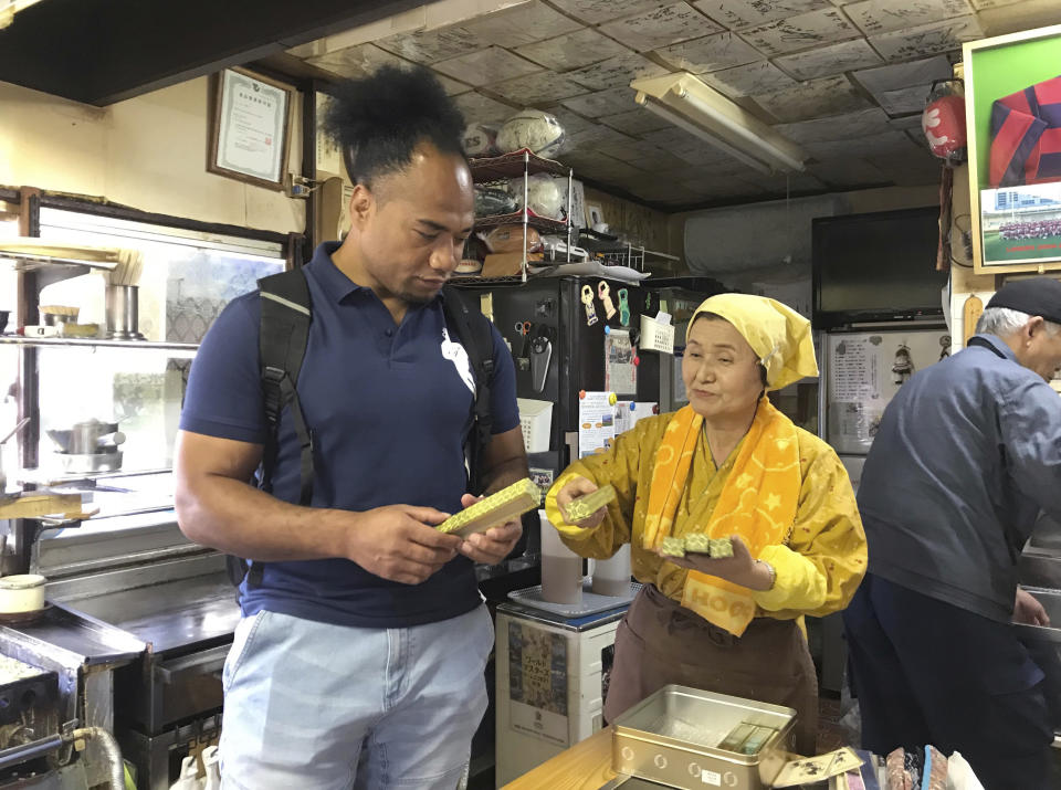 In this Friday, Oct. 26, 2018, photo, former rugby player Toetu’u Taufa and Harumi Okuno, center, co-owner of a popular Takoyaki stand, sort through paper fans near Hanazono Stadium, one of 12 venues for the 2019 Rugby World Cup, in Higashiosaka, western Japan. At a tiny stand in the shadows of the 26,500-seat stadium, Okuno serves the ubiquitous Osaka delicacy Takoyaki (Octopus filled Japanese snacks). She and her husband Hiroshi Okuno have hosted some of the sport's biggest teams including the All Blacks. (AP Photo/Jim Armstrong)