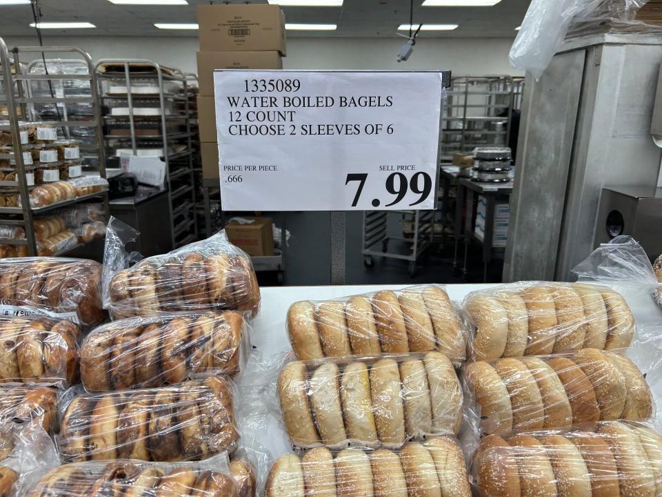 Costco's bakery section with rows of plain and flavored bagels in bags under $7.99 price sign