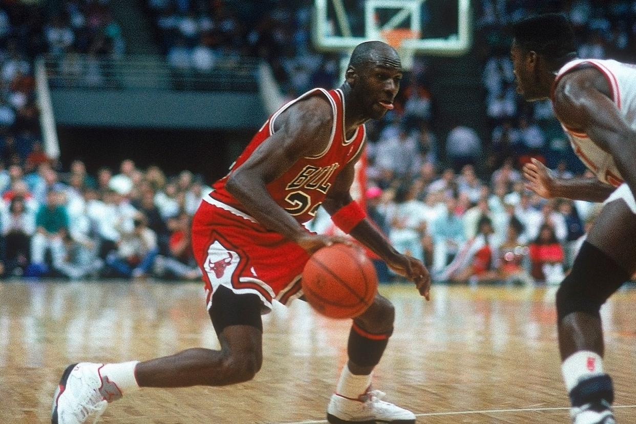 Michael Jordan dribbles towards the basket in a red Chicago Bulls uniform during a game.