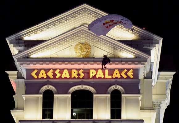 Person falling with a parachute in front of Caesars Palace location at night.