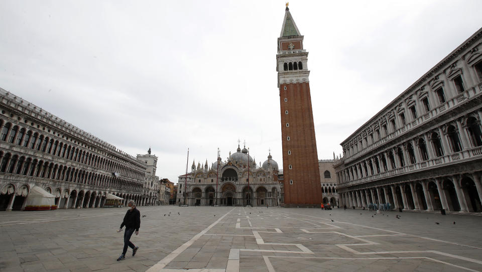 In this picture taken on Wednesday, May 13, 2020, a man wearing a sanitary mask walks in St. Mark's Square in Venice, Italy. Venetians are rethinking their city in the quiet brought by the coronavirus pandemic. For years, the unbridled success of Venice's tourism industry threatened to ruin the things that made it an attractive destination to begin with. Now the pandemic has ground to a halt Italy’s most-visited city, stopped the flow of 3 billion euros in annual tourism-related revenue and devastated the city's economy. (AP Photo/Antonio Calanni)