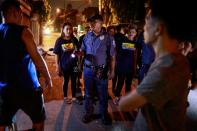 A policeman reprimands men for drinking in public, while accompanying a volunteer group of women patrollers on the streets of Pateros