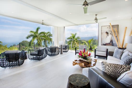 An image of a lounge room in the Tulemar Bungalows & Villas, Costa Rica, showing a view of the rainforest. The room has comfortable rattan chairs and lounge suites.
