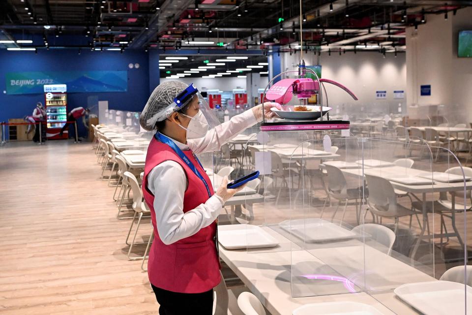 A staff member reaches for the food delivered to her robotically in the dining area during the preparation time at the Main Media Centre