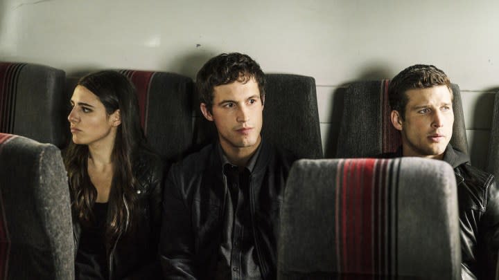 A woman and two men sit in the back of a bus in a scene from the show Imposters.