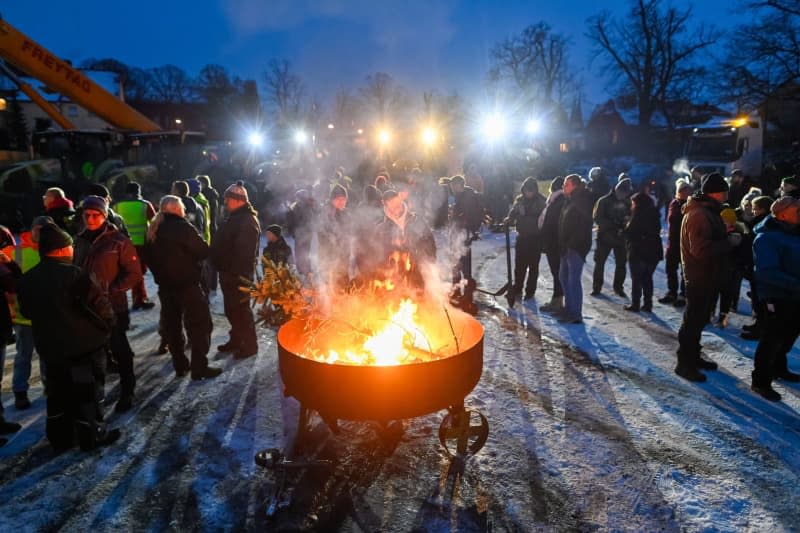 Farmers stand around a bonfire at a rally on the Schuetzenplatz in Stendal. They are protesting against the German government's austerity plans. The farmers' tractors can be seen in the background. Klaus-Dietmar Gabbert/dpa