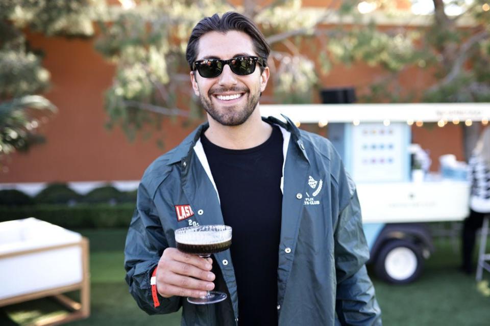 Jason Tartick wears sunglasses and holds an espresso martini outside.