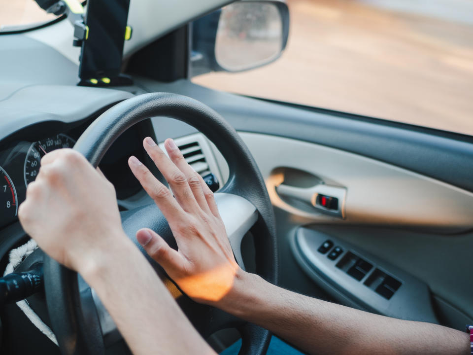 Pictured is a close up of a driver's hand pressing on a car horn while driving.