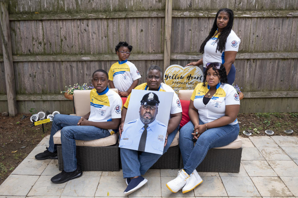 Octavia Tokley standing right, along with her mother-in-law, Ikelyn, step-daughter 21 year old Tamaira, step-son 12-year old XavierSunday, and daughter Amethyst, five years old, pose with a portrait of Erin "Toke" Tokley, a Philadelphia cop who died from COVID-19 in March, on Aug. 29, 2021, in Secane, Pa. Tokley was scheduled to be vaccinated on March 11 – which turned out to be his funeral. (AP Photo/Laurence Kesterson)