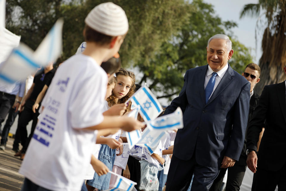 Israeli Prime Minister Benjamin Netanyahu, right, greets students as they wave Israeli flags during a ceremony opening the school year in the Jewish settlement of Elkana in the Israeli-occupied West Bank Sunday, Sep. 1, 2019. (Amir Cohen/Pool Photo via AP)