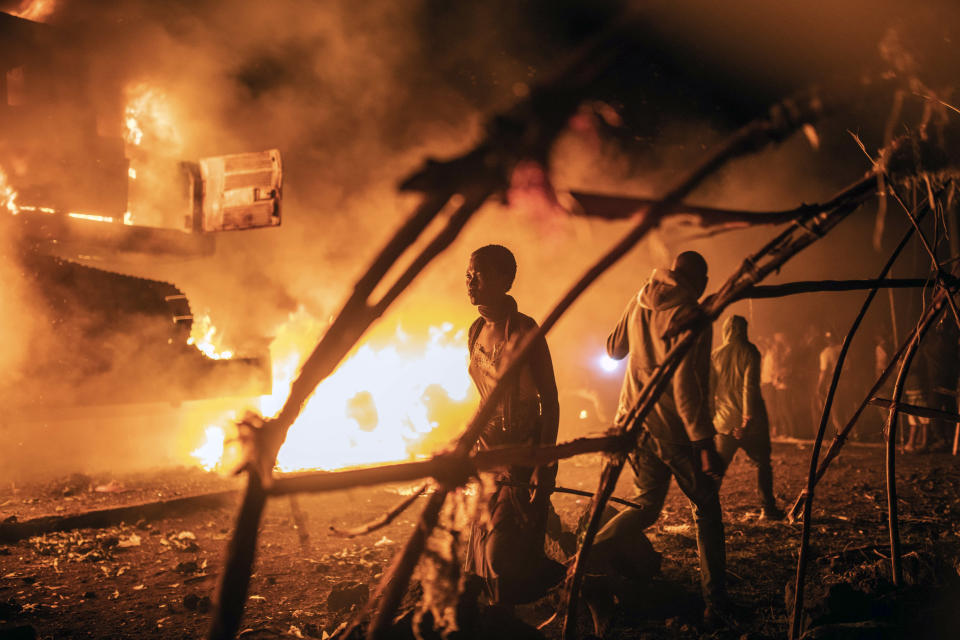 People walk by U.N. vehicles which were set on fire by angry crowds frustrated over the advance of M23 rebels, in Goma, Democratic Republic of Congo, Tuesday, Nov. 1, 2022. The violence came amid false rumors that the U.N. had transported rebels. (AP Photo/Moses Sawasawa)