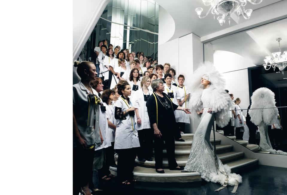 On Chanel's celebrated staircase, head dressmaker Martine Houdet (in black) admires the wedding dress she and her team created modeled by Natalia Vodianova. Chanel Haute Couture alabaster embroidered-pearl-and-strass organza dress with layers of pleated tulle, and ruffled hat with silk camellias.