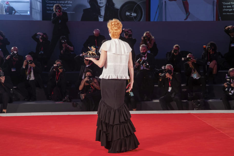 FILE - Actress Tilda Swinton poses on the red carpet with his Golden Lion For Lifetime Achievement award before a group of adequately-spaced media members rtduring the opening ceremony of the 77th edition of the Venice Film Festival at the Venice Lido, Italy, on Sept. 2, 2020. This year, three of the four major fall film festivals, including Venice, are going forward despite the pandemic. Those in Venice acknowledge it hasn’t been anywhere near the same. Masked moviegoers in set-apart seats. A barrier walls off the red carpet to discourage crowds of onlookers. Greetings are kiss-less. A little bit of the romance of movies has gone out. (AP Photo/Domenico Stinellis, File)