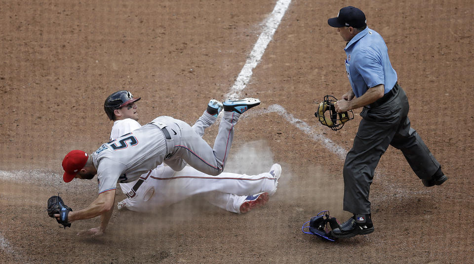 Atlanta Braves' Austin Riley, center, slides into home plate as Miami Marlins' Anthony Bass, left, topples over him during the 10th inning of a baseball game Sunday, July 4, 2021, in Atlanta. After a review of the play, the ruling on the field was overturned and Riley was called out. (AP Photo/Ben Margot)