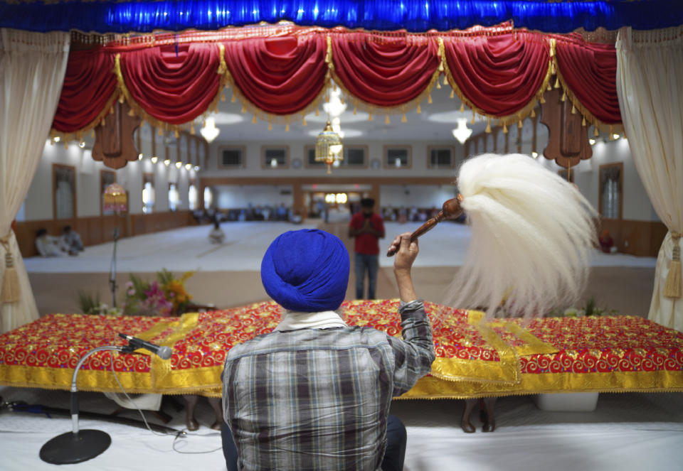 A man waves the Chaur Sahib, paying respect to the sacred scripture, during evening prayer at Gurdwara Millwoods, a Sikh house of worship, in Edmonton, Alberta, on Wednesday, July 20, 2022. (AP Photo/Jessie Wardarski)