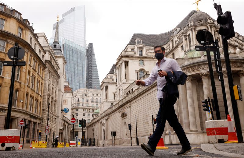 FILE PHOTO: A man wearing a face mask crosses the road in the City of London financial district amid the outbreak of the coronavirus disease (COVID-19)