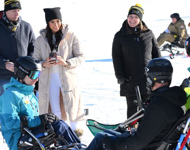 <p>Karwai Tang/WireImage</p> Meghan Markle takes a photo of Prince Harry sit-skiing in Canada on Feb. 14, 2024