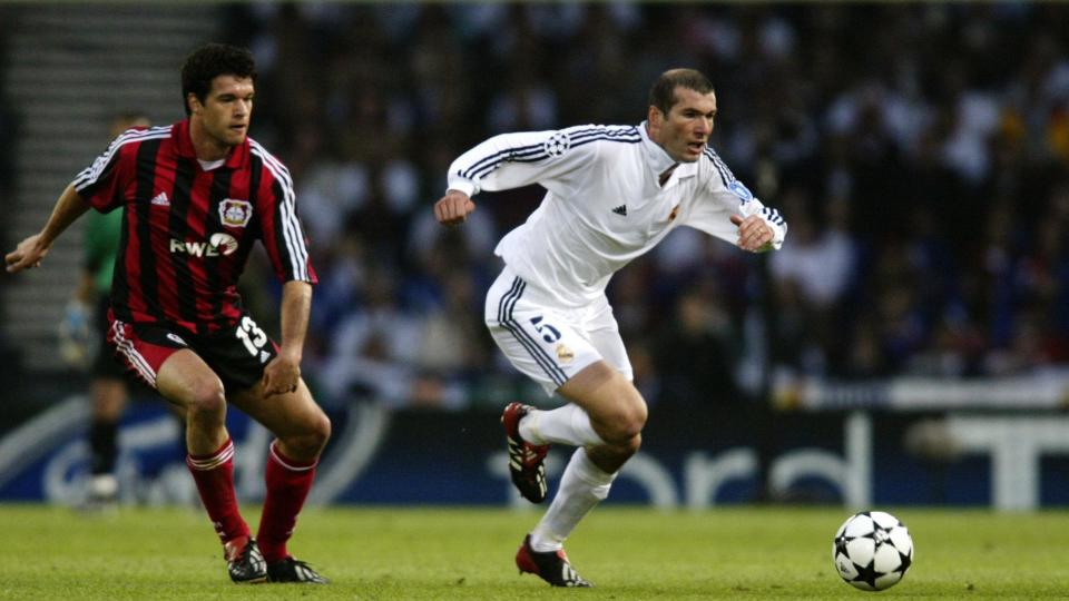 Two footballers in game one wearing all white kit the other wearing black and red striped, the ball is ahead of them it is white with black stars on it