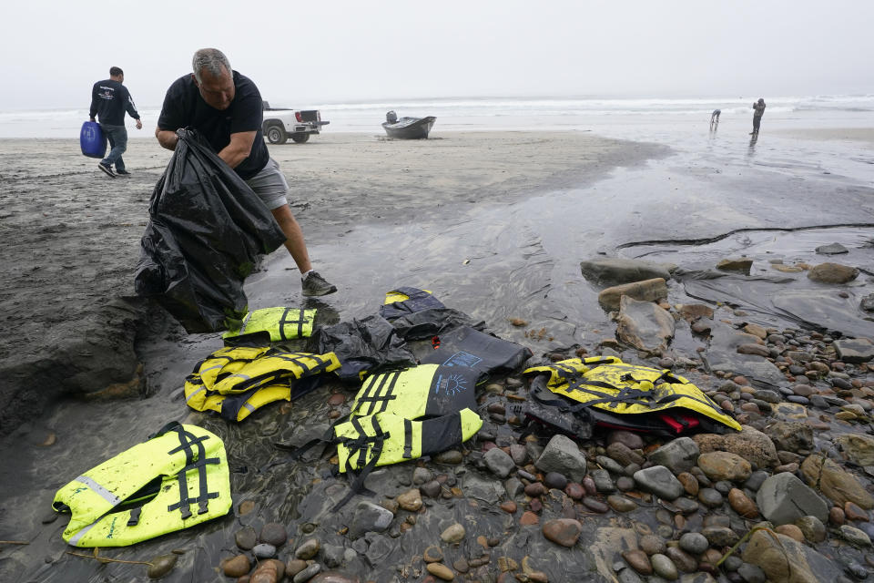 FILE - Boat salvager Robert Butler places life preservers in a plastic bag in front of one of two boats that capsized in shallow but turbulent surf off the San Diego coast, on Blacks Beach, March 12, 2023. At least seven of eight people killed when the two boats capsized were Mexican migrants, Mexican officials. (AP Photo/Gregory Bull, File)