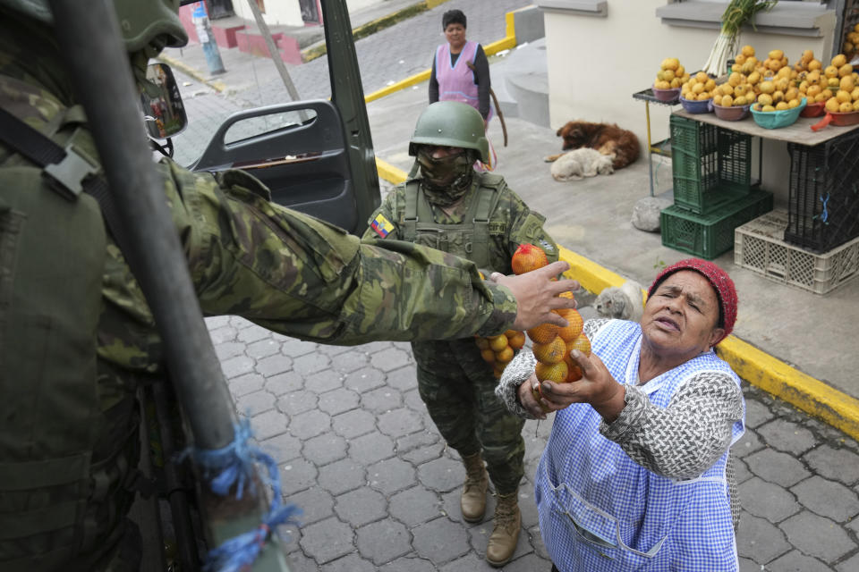 Una vendedora de fruta obsequia unas naranjas a los militares mientras patrullan por el sur de Quito, Ecuador, el viernes 12 de enero de 2024, como secuela a la fuga de dos cabecillas de bandas criminales de prisión. El presidente Daniel Noboa decretó el lunes el estado de emergencia nacional debido a una ola de criminalidad, una medida que permite a las autoridades suspender los derechos de las personas y movilizar a los militares. El gobierno también impuso un toque de queda. (Foto AP/Dolores Ochoa)