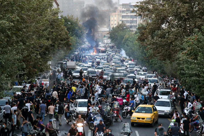 Dozens of demonstrators stand in the street as cars are forced to go around them.