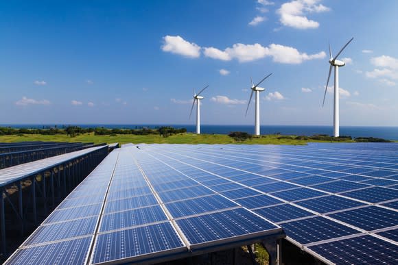 A solar farm with wind turbines in the distance.