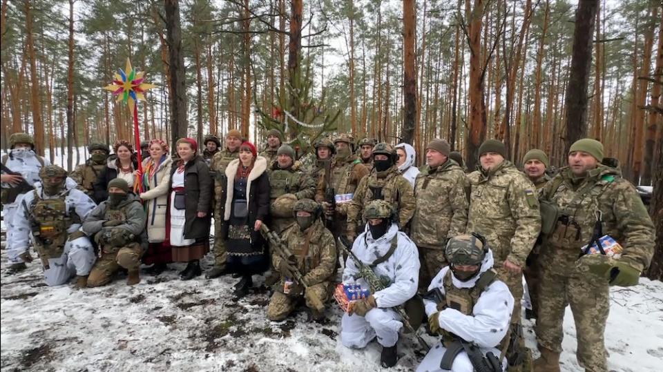 A group of Ukrainian soldiers in northern Ukraine stand with a group of singers in a snowy wood on December 25, 2023.