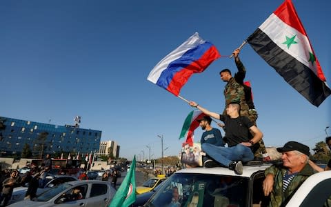 Syrians wave Russian and Syrian flags during a protest against U.S.-led air strikes in Damascus - Credit: Reuters