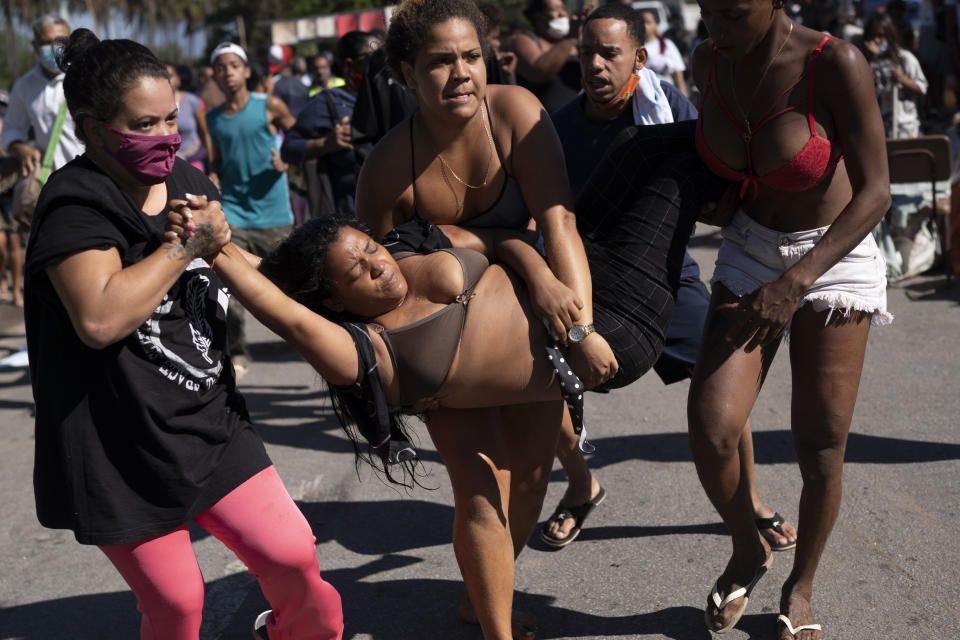 A woman who fainted during an eviction is carried away from the crowd for medical attention as they are evicted from land designated for a Petrobras refinery, where a settlement coined the "First of May Refugee Camp," was created, the name referring to the date people moved here and set up tents and shacks to live in during the new coronavirus pandemic in Itaguai, Rio de Janeiro state, Brazil, Thursday, July 1, 2021. (AP Photo/Silvia Izquierdo)