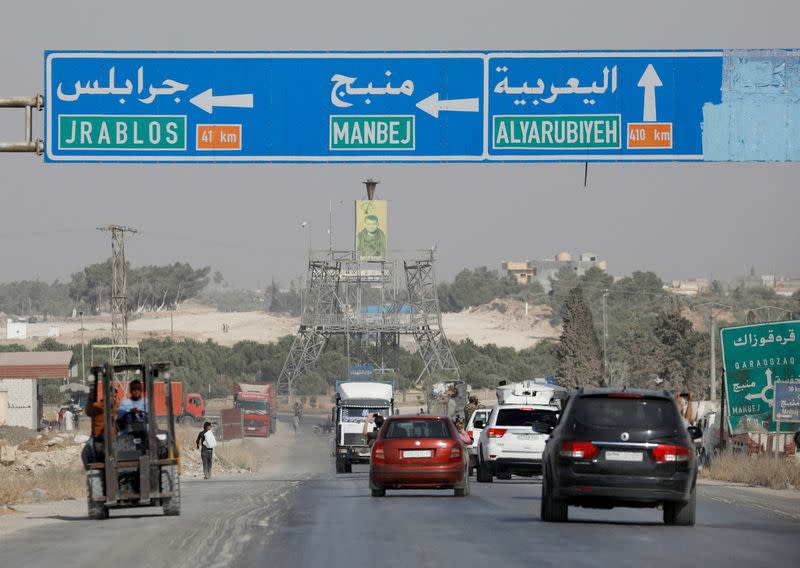 FILE PHOTO: Cars pass under a road sign that shows the direction to Manbij city, at the entrance of Manbij