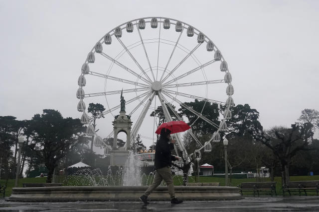 A pedestrian carries an umbrella while walking past the SkyStar Observation Wheel in Golden Gate Park in San Francisco, Tuesday, March 21, 2023. (AP Photo/Jeff Chiu)