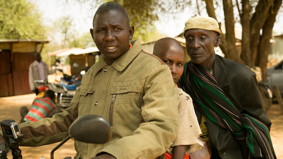 Pkoror Lomerilima, center, sits on a motorbike between his father, right, and&nbsp;community mobilizer&nbsp;Isaac Nyeris, left. (Photo: Zoe Flood)