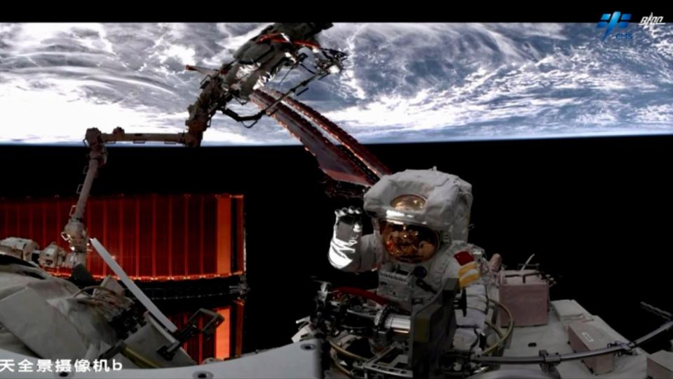 a chinese astronaut on a spacewalk waves to the camera with earth in the background