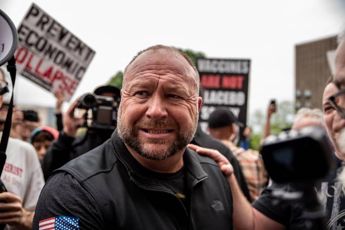 Man in black shirt and hat at outdoor protest with signs and people around