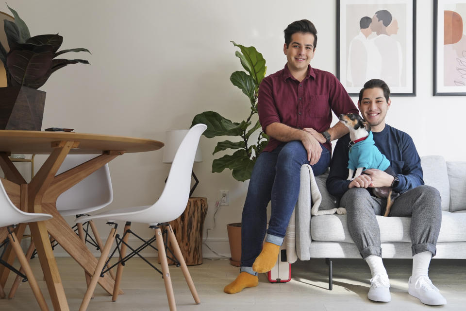 In this Monday, Nov. 25, 2019 photo, Zachariah Mohammed, left, Pete Mancilla, and their dog Remy pose for a picture in their apartment in New York. Most of the furniture in their apartment, including the couch, the table and chairs, the side table and the bar cart, are rented. Furniture-rental startups and other companies are aiming to rent furniture to millennials who don't want to commit to big purchases or move heavy furniture and are willing to pay for the convenience. (AP Photo/Seth Wenig)