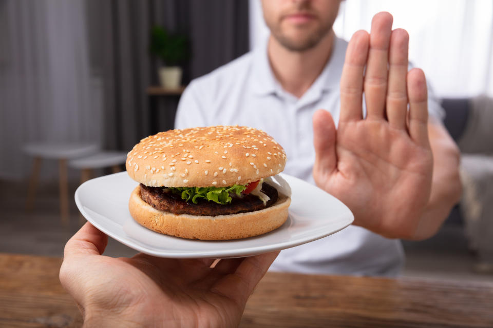 A Close-up Of A Man's Hand Refusing Burger on a white plate Offered By Person