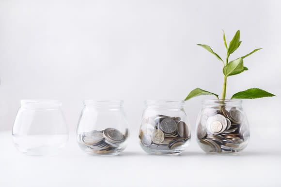 A series of glass jars, each with successively more coins than the last, and a plant sprouting out of the last jar.