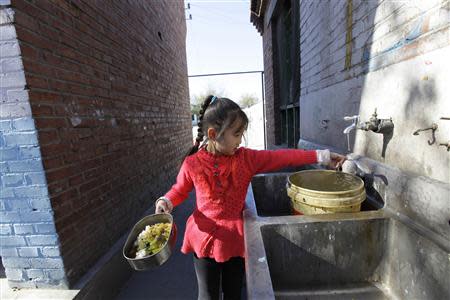 A student washes a spoon as she holds her container of food for lunch at Pengying School on the outskirts of Beijing November 11, 2013. REUTERS/Jason Lee