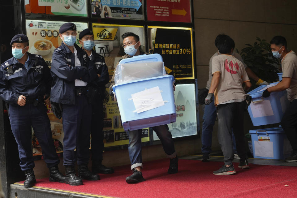 Workers carry some evidences walks past police officers outside office of "Stand News" in Hong Kong Wednesday, Dec. 29, 2021. Hong Kong police raided the office of the online news outlet on Wednesday after arresting several people for conspiracy to publish a seditious publication. (AP Photo/Vincent Yu)