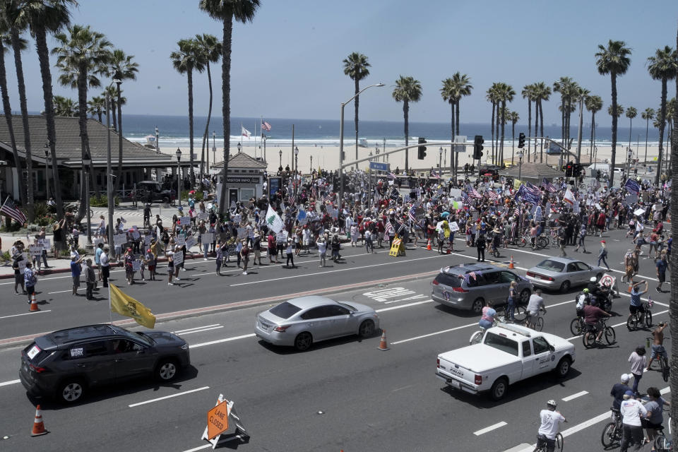 Protesters hold signs and wave flags in a demonstration on May Day during the coronavirus pandemic at the pier, Friday, May 1, 2020, in Huntington Beach, Calif. (AP Photo/Chris Carlso