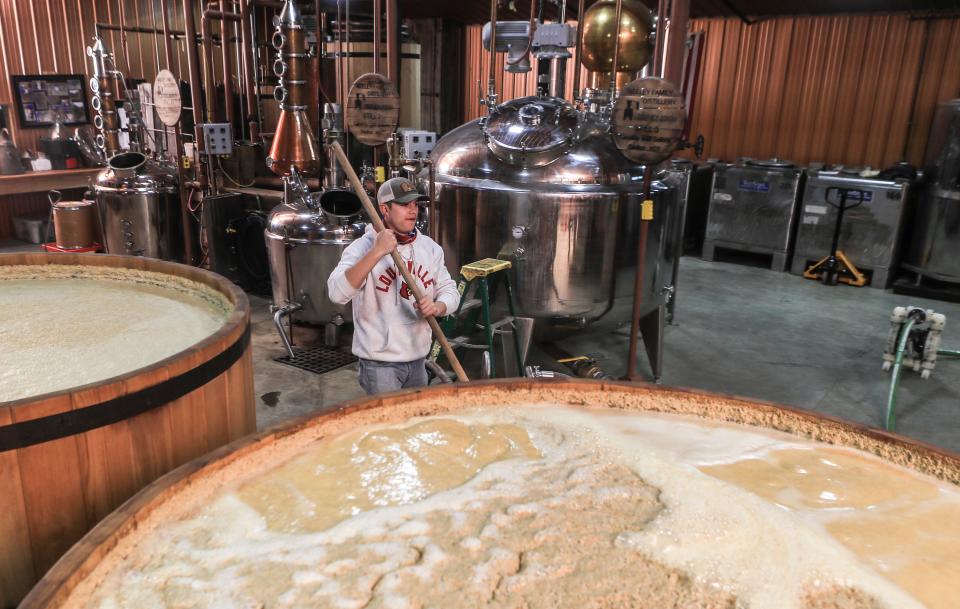 Assistant distiller Grant Cobb carries a wooden mixer while working in the distillery recently. The fermenters in the foreground are made from cypress wood; they're resistant to rot and don't flavor the whiskey. They're also the traditional material used for bourbon-making.