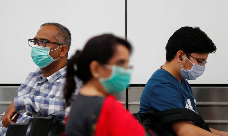 Passengers wearing protective masks sit at an airport terminal following an outbreak of the coronavirus disease (COVID-19), in New Delhi