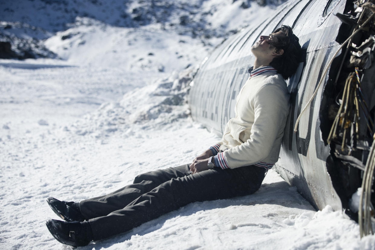  Enzo Vogrincic Roldán as a despondent Numa Turcatti sitting on a snowy mountaintop against the crashed remains of a commercial airplane in Society of the Snow. 