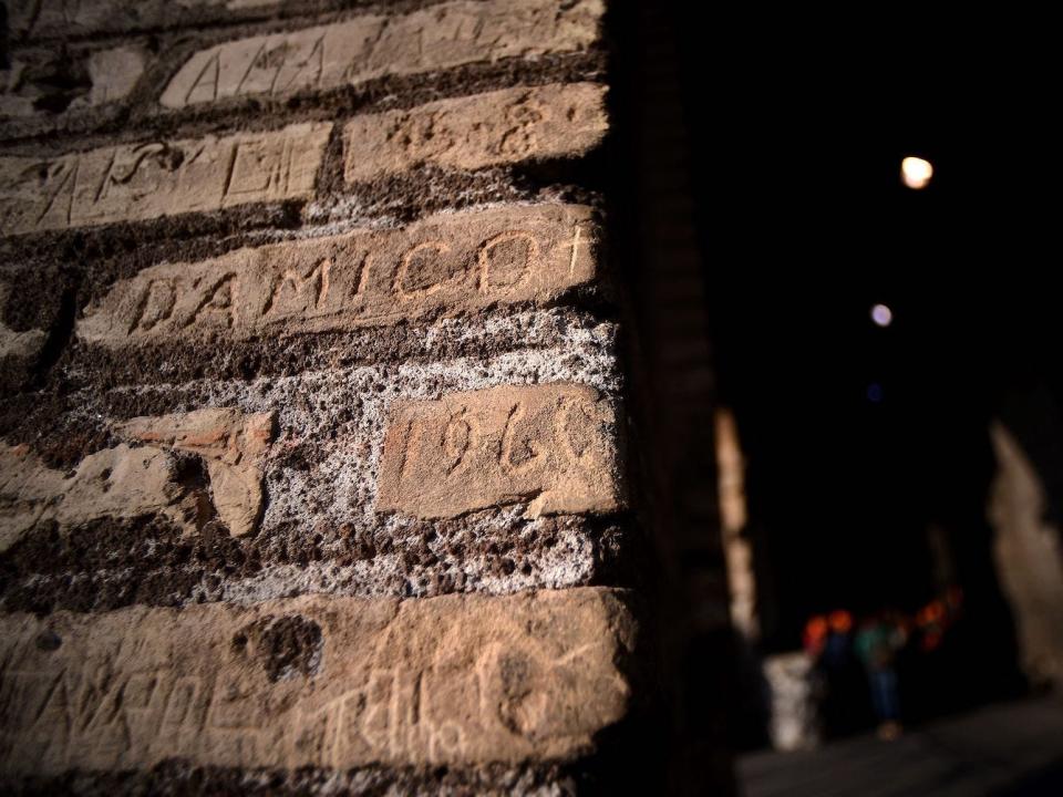 A wall of the Colosseum where several names and words have been etched into bricks in the wall.